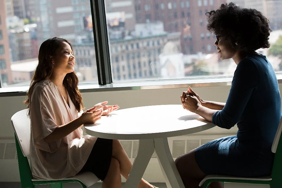 A one-to-one advisory conversation at a table beside a window overlooking the city